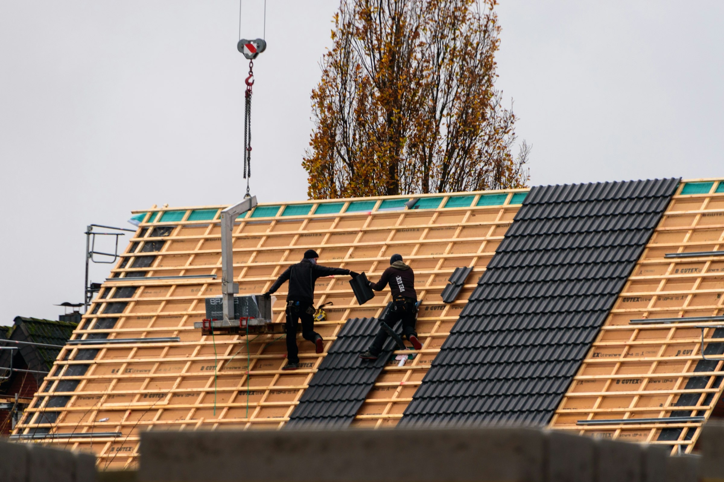 Twee dakdekkers leggen pannen op het dak van een nieuwbouwhuis in de herfst